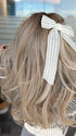 Roxie wearing BROOKLYN by BELLE TRESS in color MILKSHAKE BLONDE R | Mixture of Light sandy brown, highlighted with light ash blonde with a hint of light platinum blonde with medium root color. (styled with bow - not included)